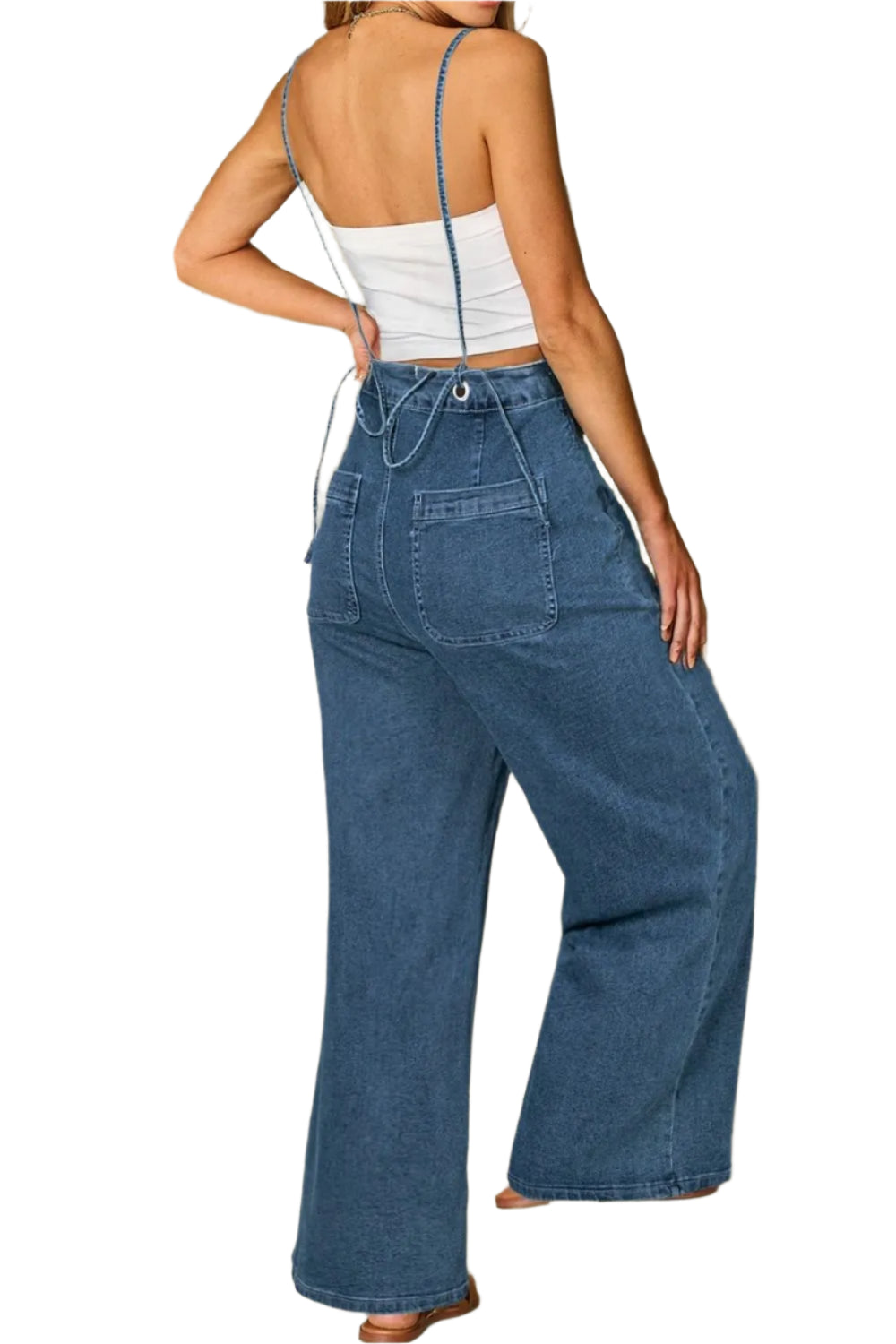 A woman wearing a white strapless top and high-waisted, wide-leg blue denim jeans, seen from the back. The jeans have large back pockets and a relaxed fit, while the top features thin blue straps that cross over the shoulders.