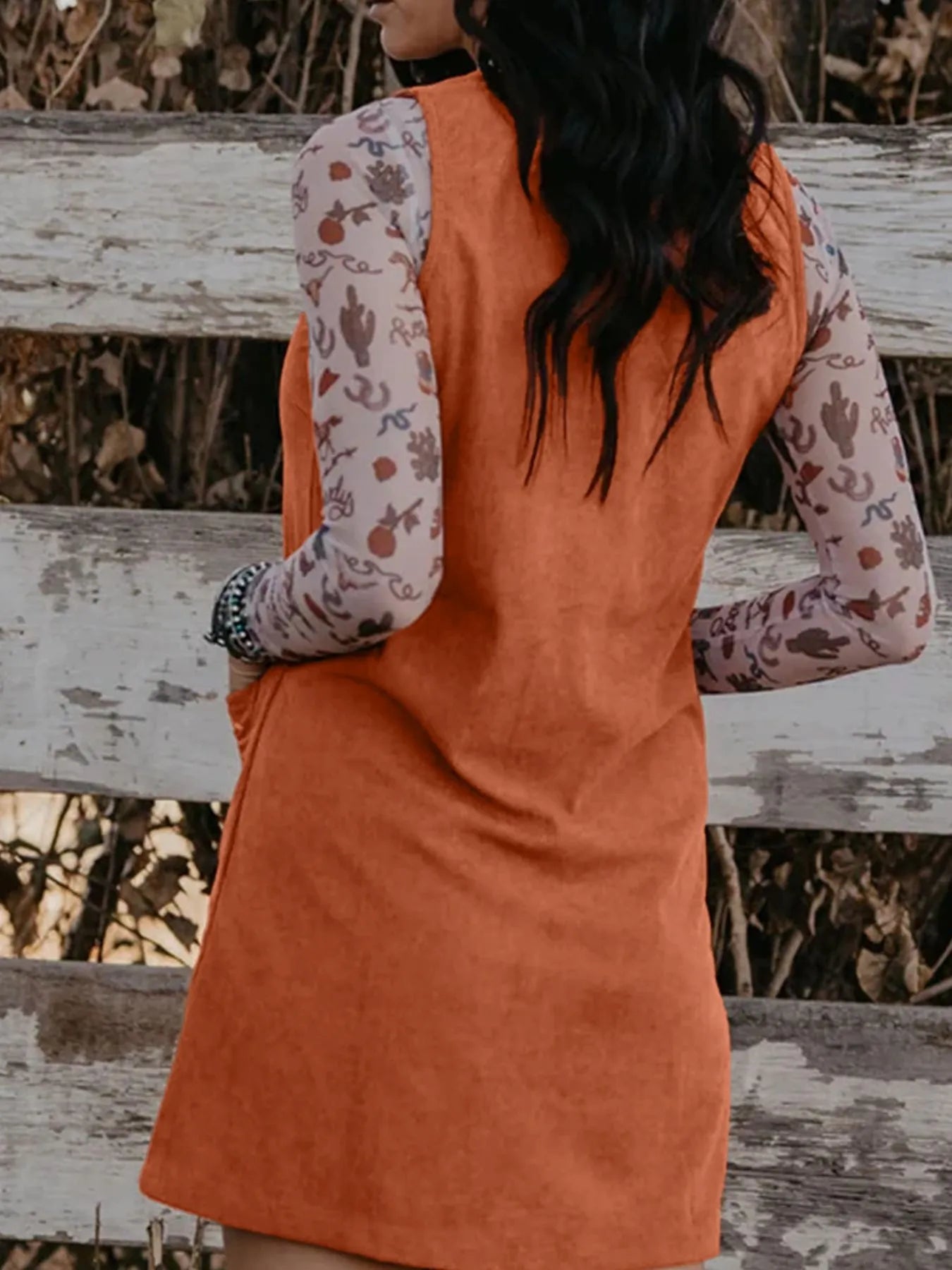 Back view of a rust orange sleeveless corduroy mini dress paired with a printed mesh top, styled for a western-inspired casual day look – perfect for autumn outfit ideas for women.