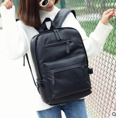 Person holding a black backpack against a chain-link fence background
