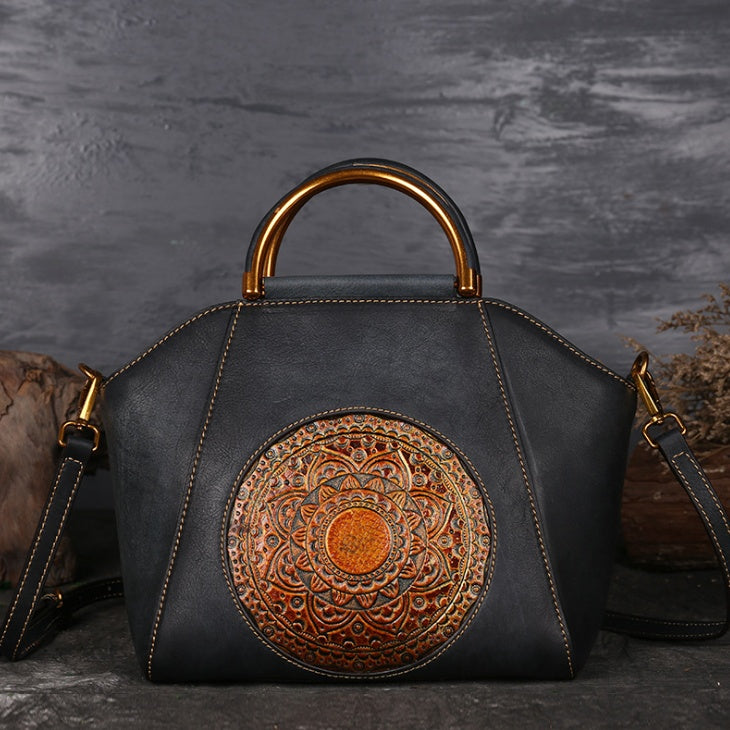 Black leather handbag with gold handle and decorative circular patch on a dark background