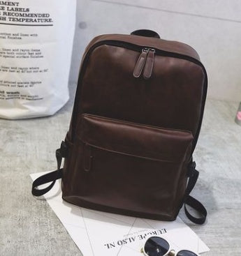 Brown backpack on a light gray surface with a white paper in the background