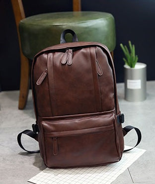 Brown leather backpack on a light gray surface with a dark background
