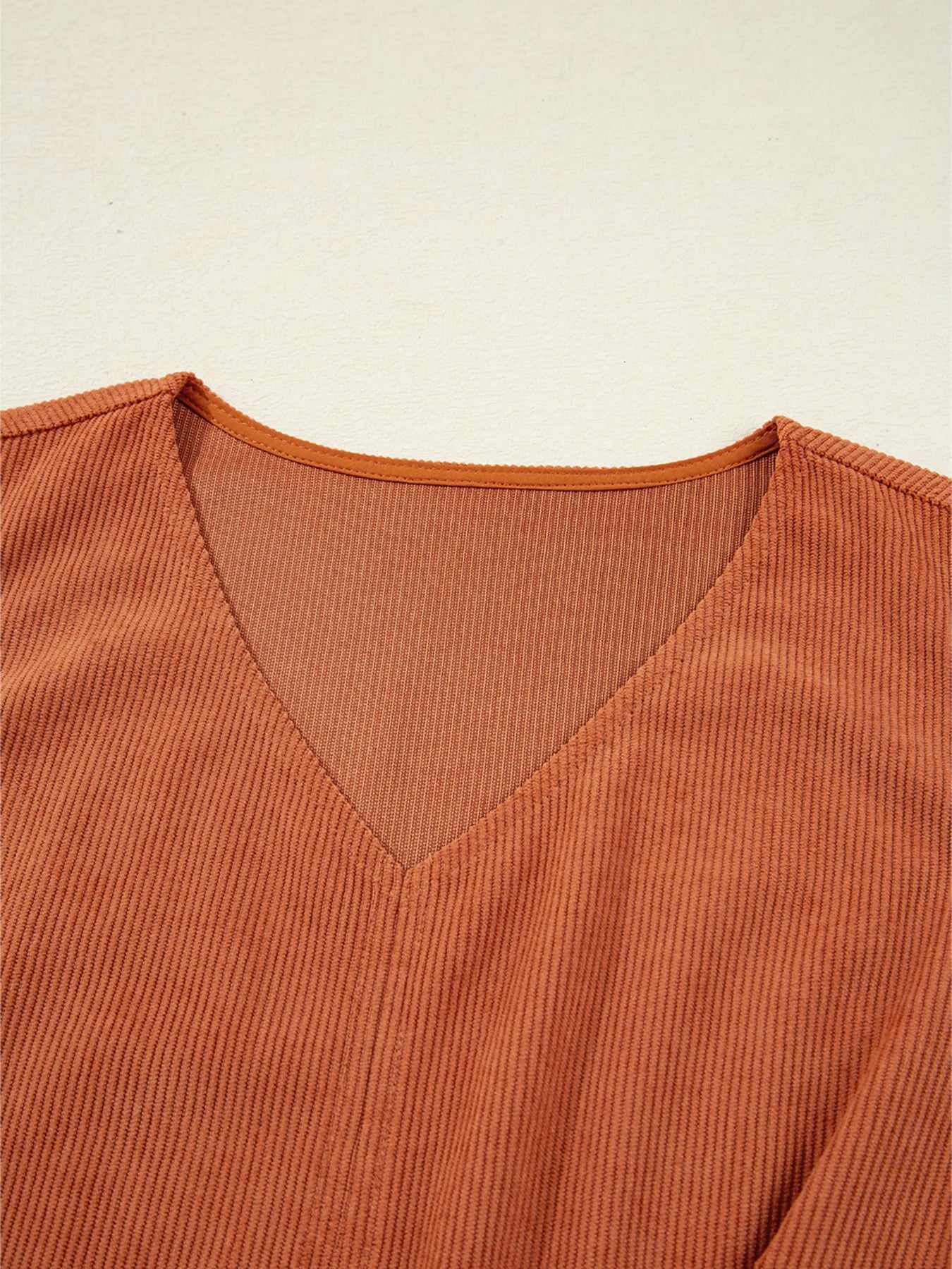 Detailed close-up of V-neckline stitching on rust-colored corduroy fabric, highlighting the fine ribbed texture and quality finish of the sleeveless women's mini dress – stylish pick for fall and winter.