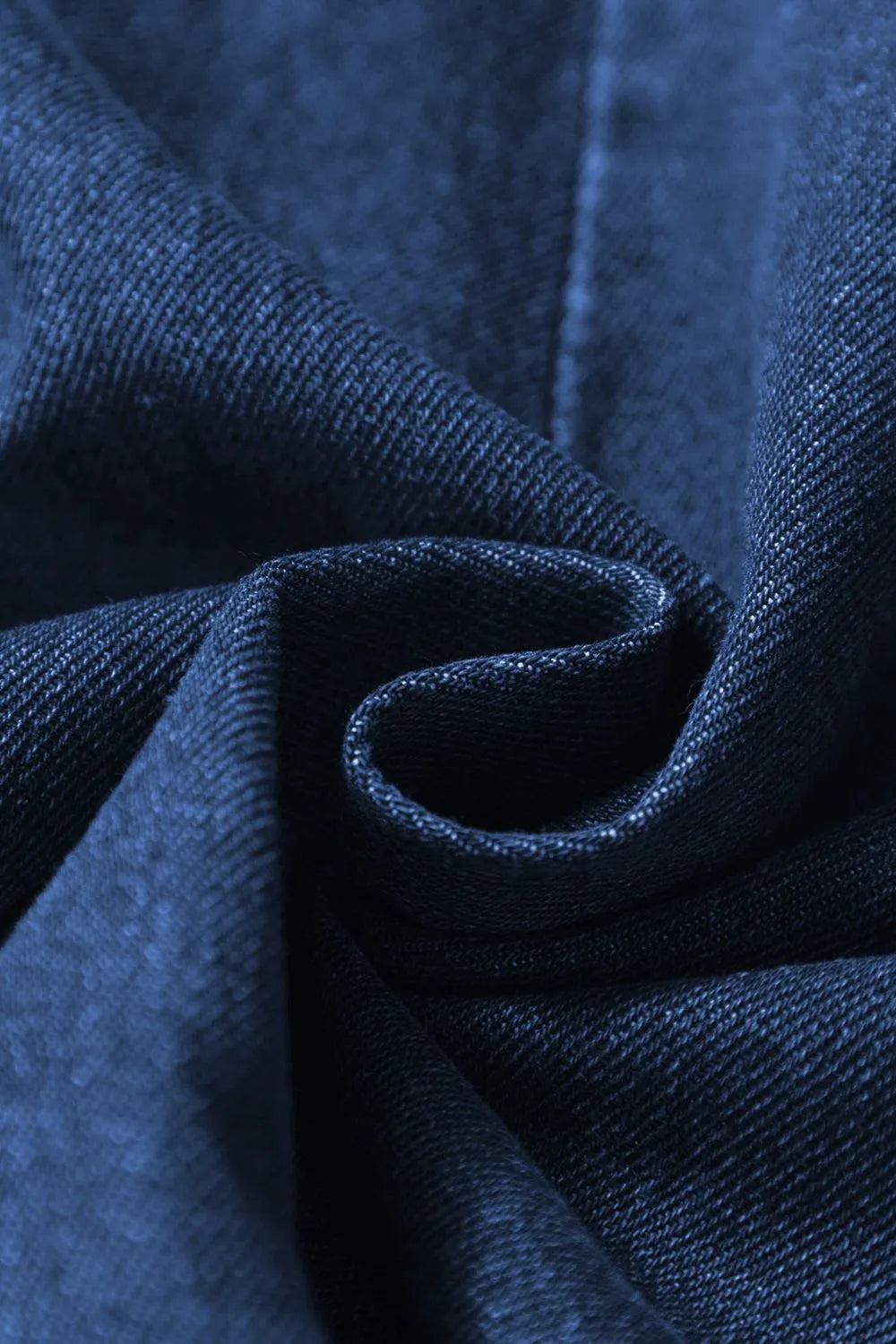 Close-up of blue denim fabric twisted into a swirl, showing detailed texture and stitching.