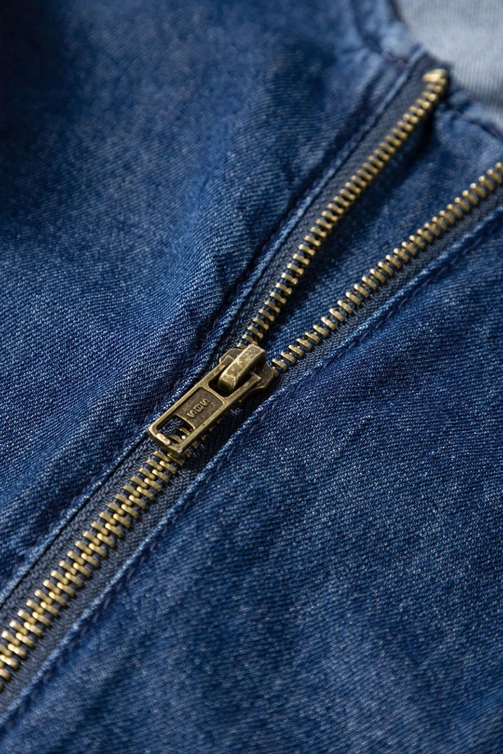 Close-up view of the gold zipper on a blue denim romper, highlighting the stitching and denim fabric detail