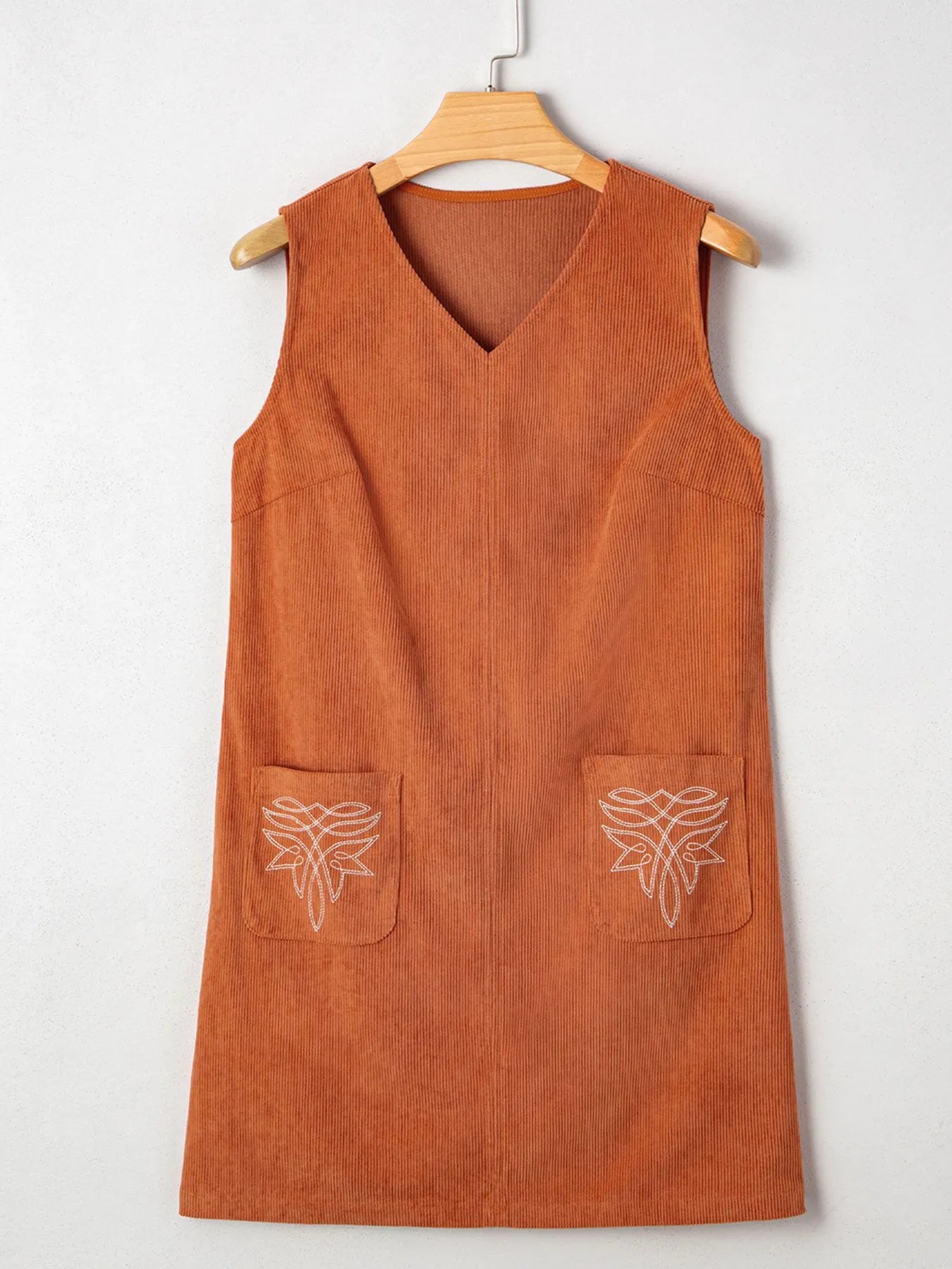 Flat lay of rust orange corduroy mini dress featuring sleeveless cut, V-neckline, and floral embroidery on front pockets – ideal for women's casual wear.