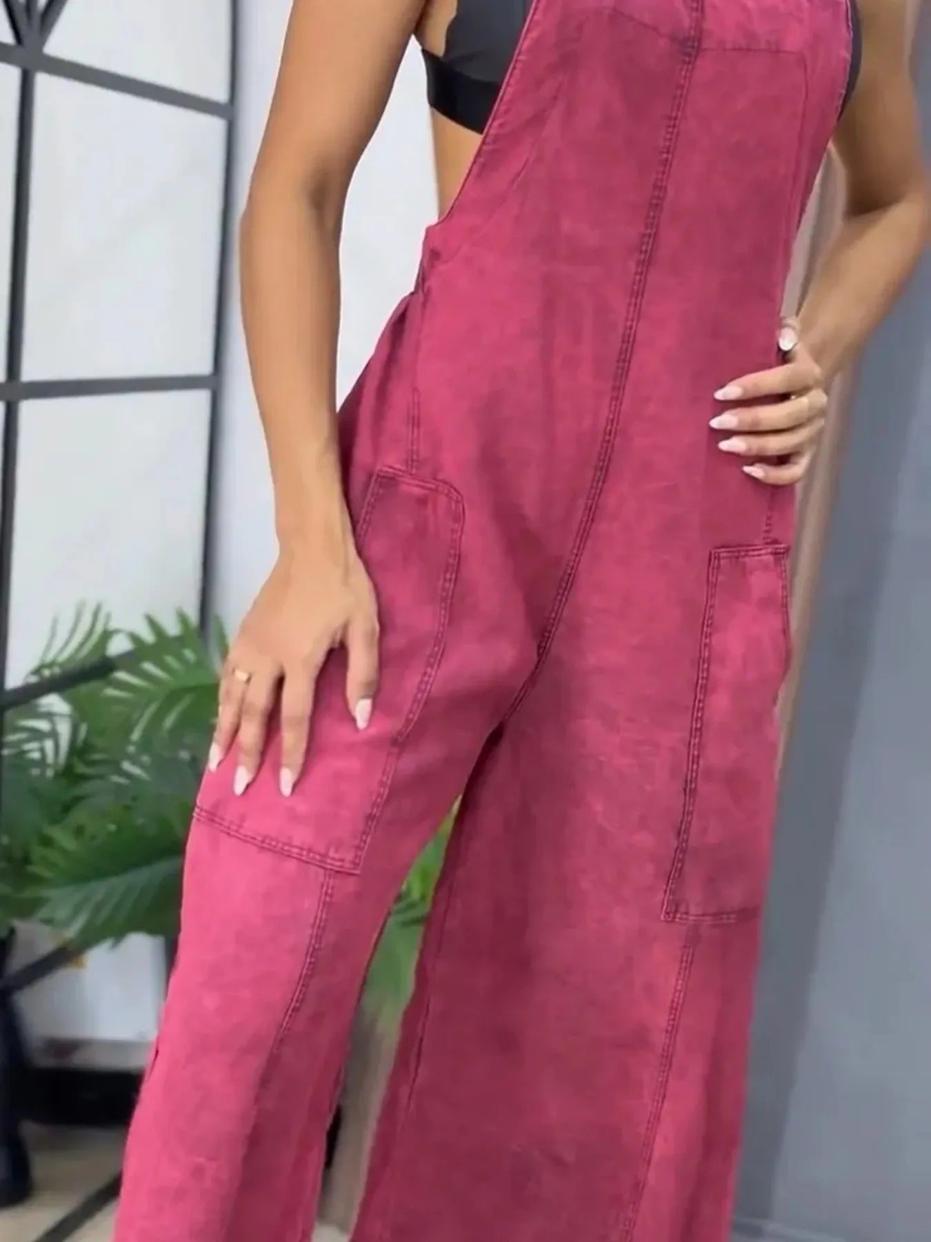 Close-up of magenta wide-leg overalls with front patch pockets, showing the details as the woman stands with her hand on her hip.