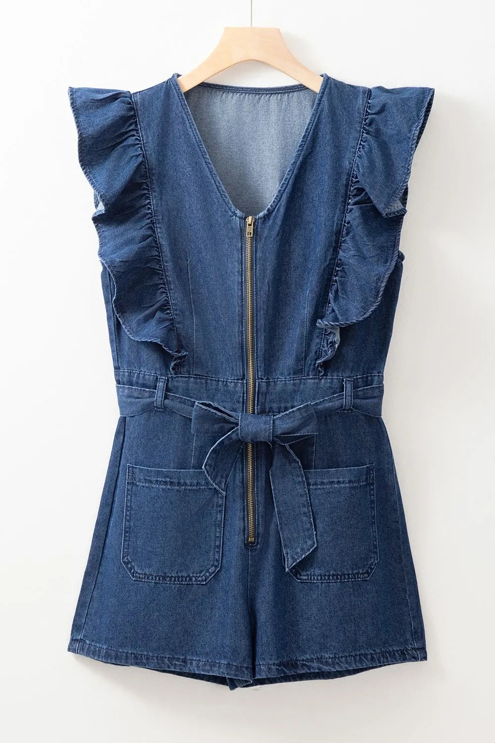 Denim romper with ruffle sleeves, front zipper, waist tie belt, and large front pockets displayed on a hanger against a white background