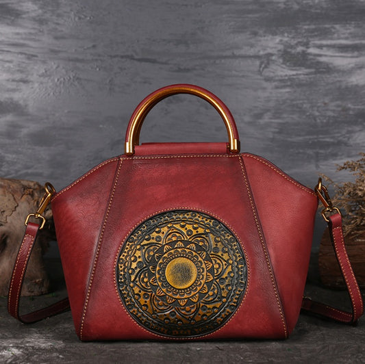 Red handbag with gold handle and decorative emblem on a textured gray background