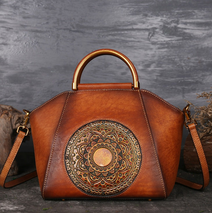 Brown leather handbag with gold embossed design on a textured gray background