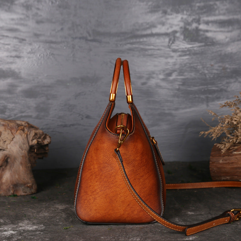 Brown leather handbag with gold accents on a dark textured surface
