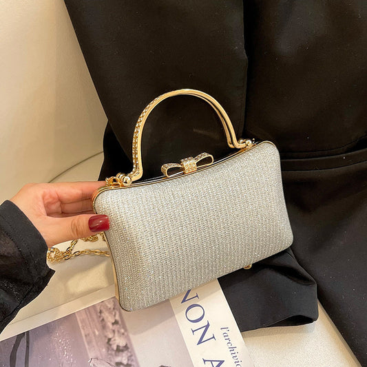 Silver handbag with gold handle held by a person wearing a black coat.