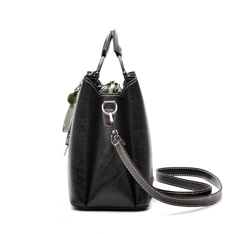 Side view of a black faux leather women's handbag with a detachable shoulder strap and visible white stitching.