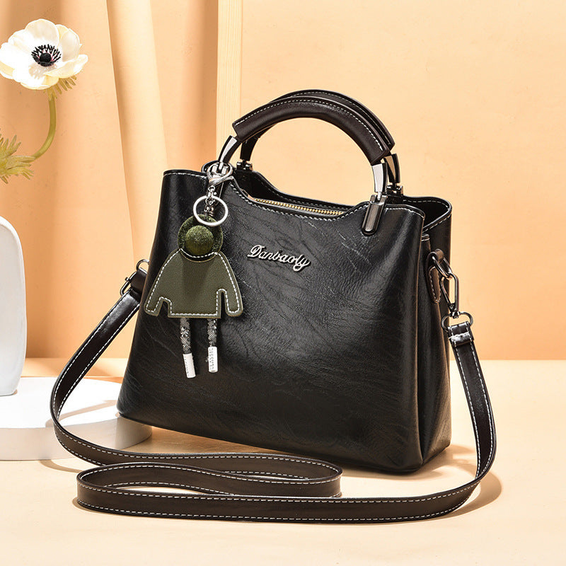 Elegant black faux leather women's handbag with top handle and detachable strap, styled with a doll-shaped keychain, displayed against a peach background