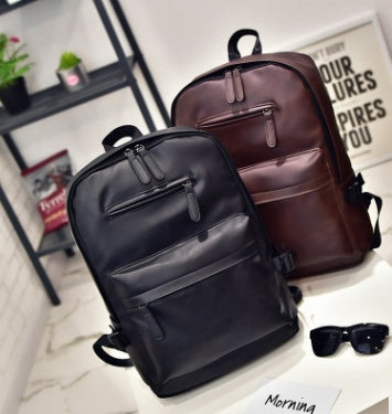 Two backpacks, one black and one brown, on a light surface with sunglasses and a plant in the background.