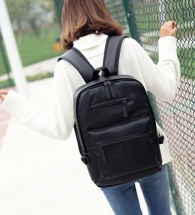 Person wearing a black backpack outdoors near a fence
