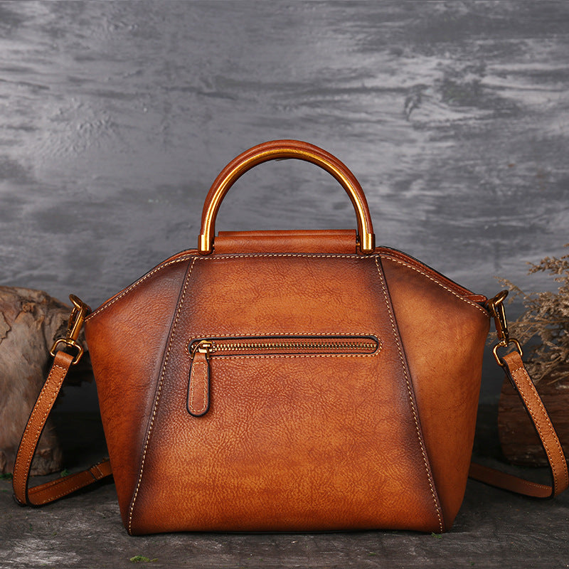 Brown leather handbag with gold accents on a textured gray background