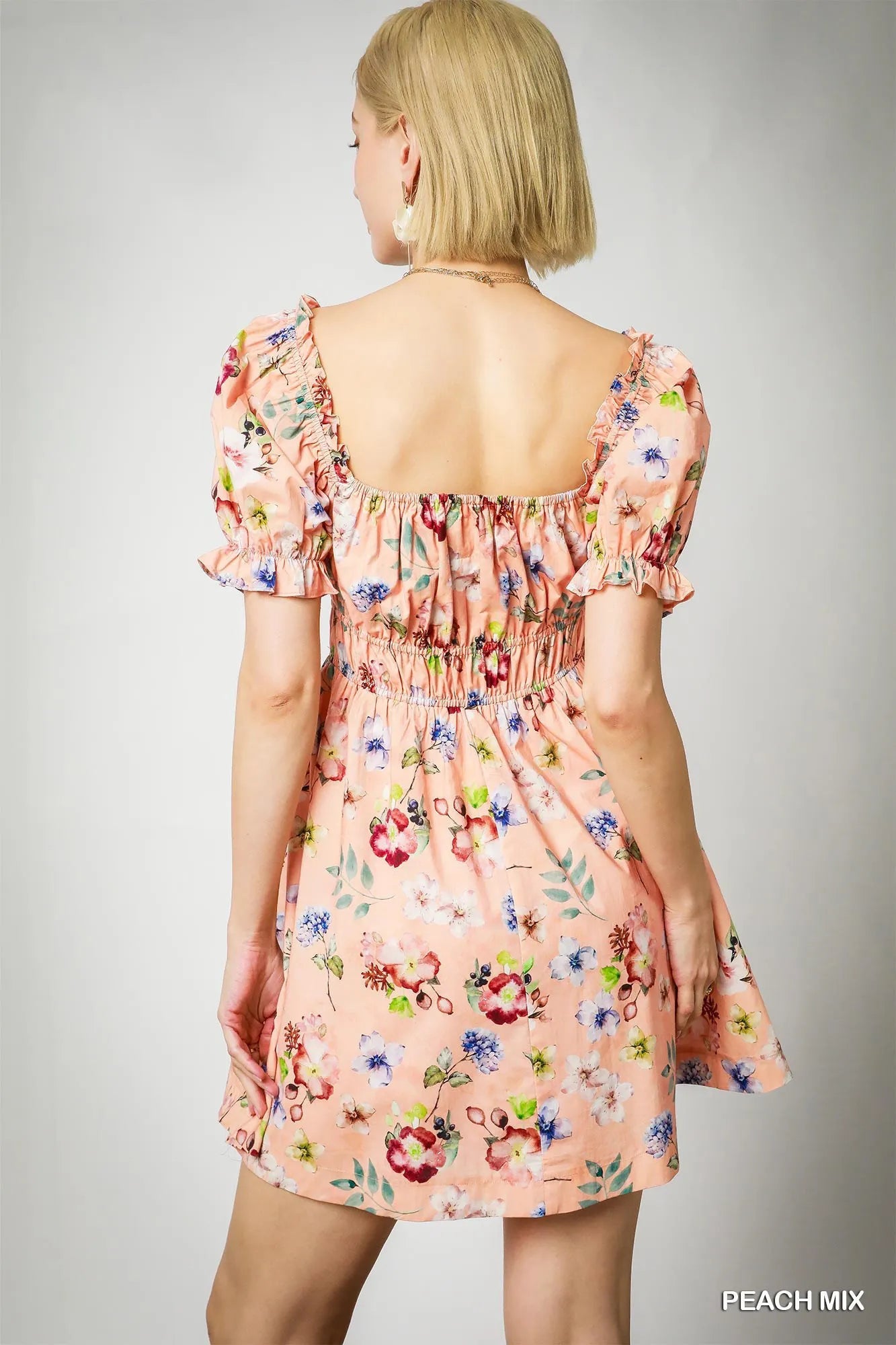 Back view of woman wearing a peach floral ruched mini dress with shirred waist and puff sleeves.
