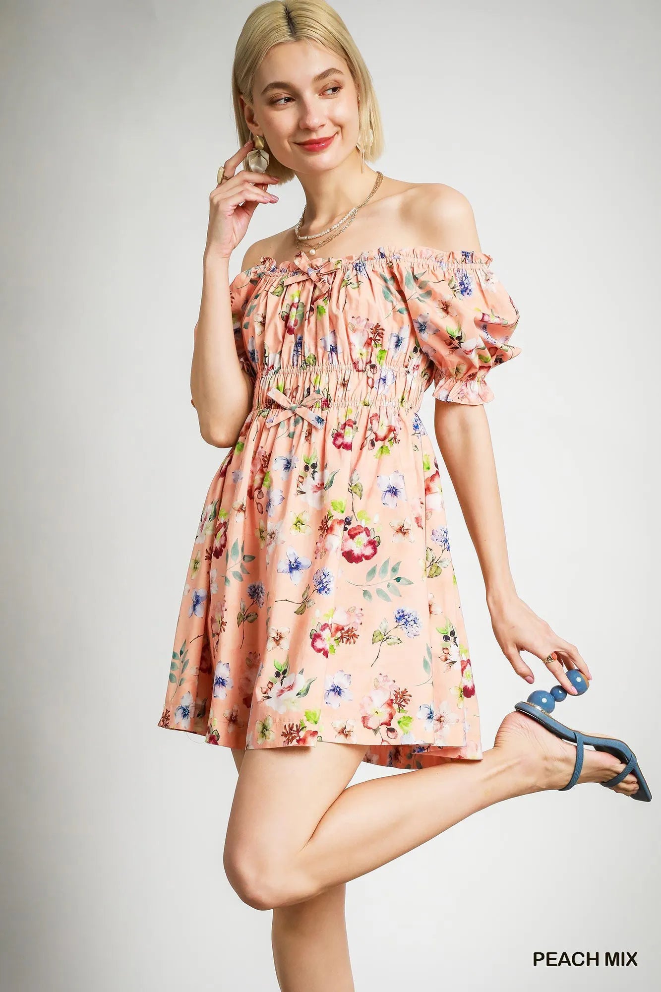 Blonde model showcasing off-shoulder look of peach floral mini dress with ruffle detailing – elegant floral fashion for women around the globe.