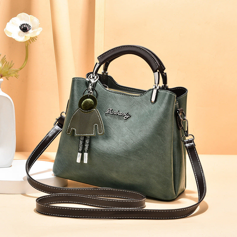 Trendy green faux leather women's handbag featuring a top handle, adjustable shoulder strap, and a cute green doll keychain, styled against a neutral peach backdrop.