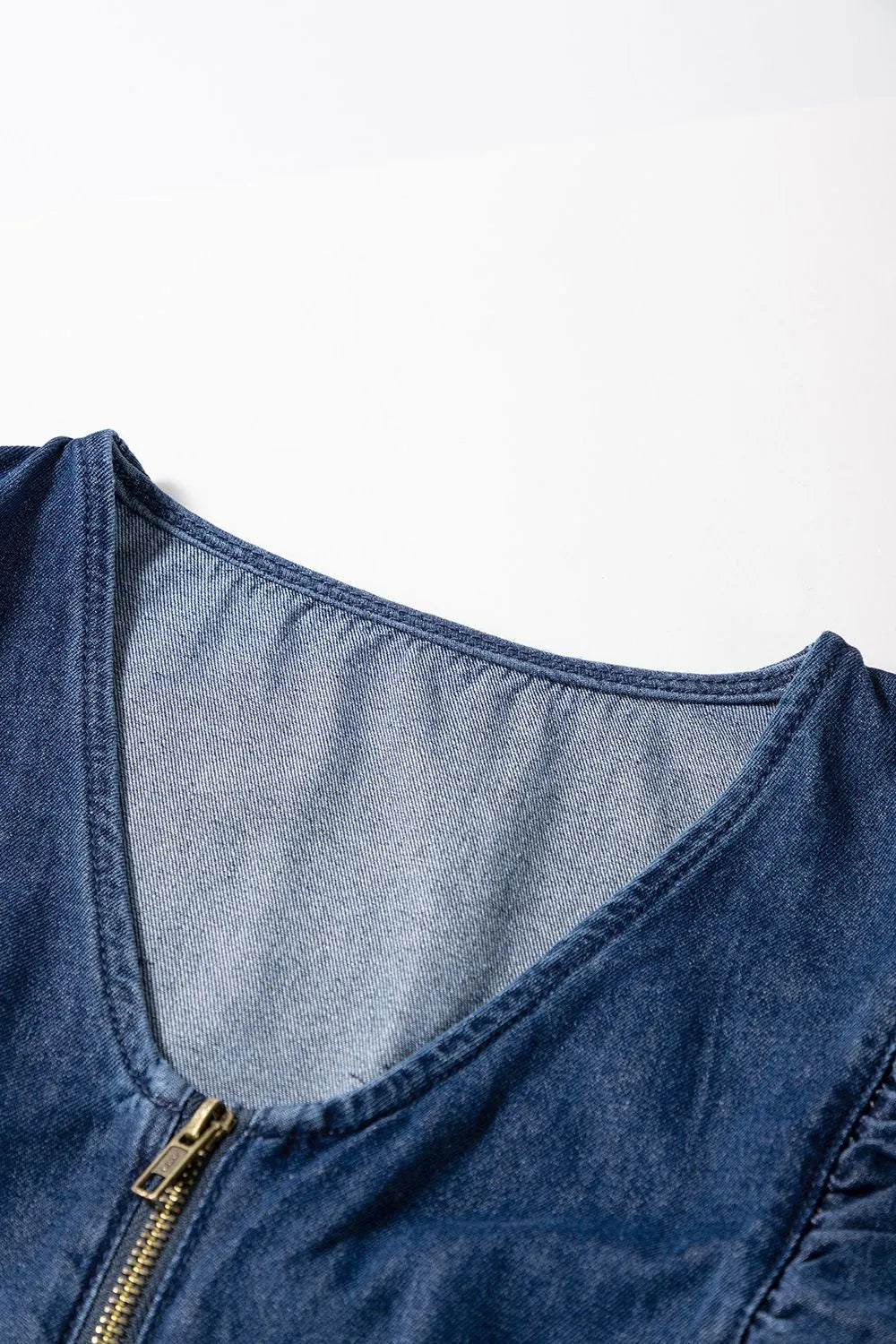 Close-up of the upper neckline and ruffle sleeve detail of a blue denim romper, showing the zipper and fabric texture