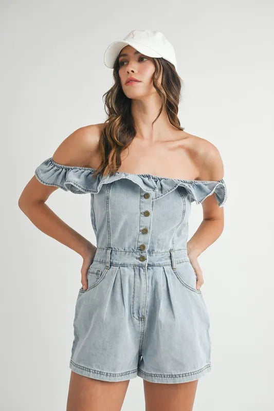 Woman wearing an off-shoulder light wash denim romper with front buttons and ruffle neckline, styled with a white cap.