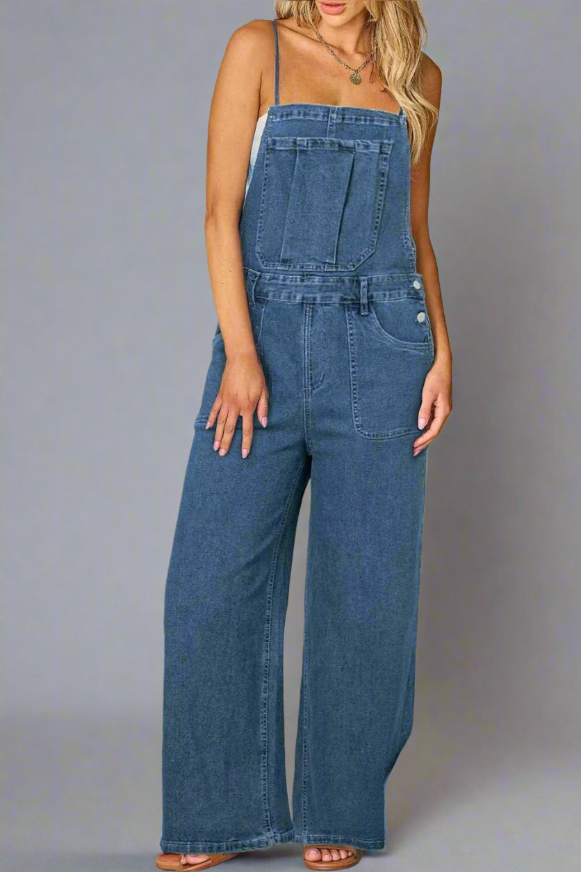 A woman wearing a sleeveless denim overall jumpsuit with wide-leg pants and front pockets. The overalls feature thin shoulder straps and a relaxed, casual fit.